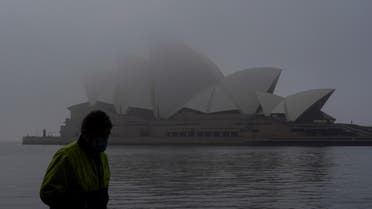 A man wearing a protective face mask walks past the Sydney Opera House, seen shrouded in fog, during a lockdown to curb the spread of a coronavirus disease (COVID-19) outbreak in Sydney, Australia, July 1, 2021. (Reuters)