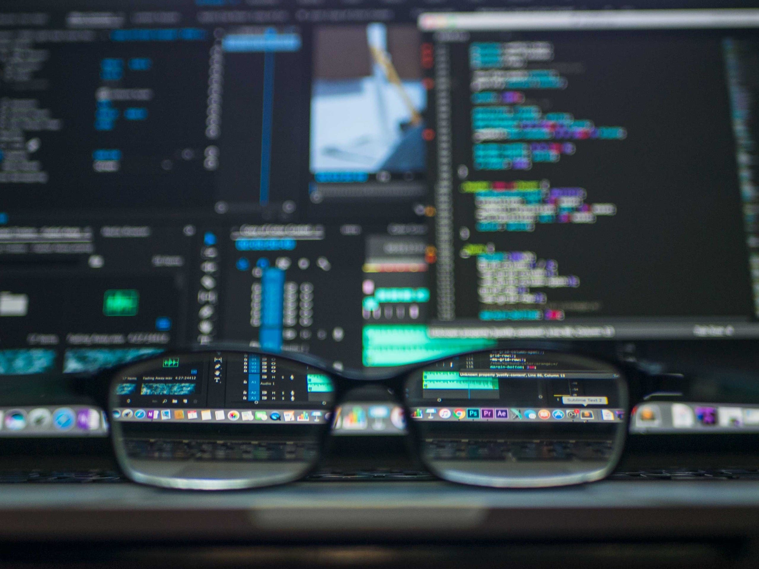 Glasses placed on a desk with a computer monitor in the background. (Unsplash, Kevin Ku)