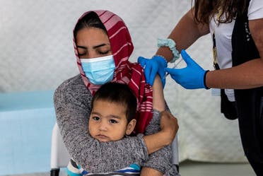 A migrant holds her baby as she receives a shot of the Johnson & Johnson vaccine against the coronavirus in the Mavrovouni camp for refugees and migrants on the island of Lesbos, Greece, on June 3, 2021. (Reuters)