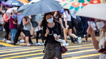 A woman (C) holds an umbrella as she crosses a road in Hong Kong on July 20, 2021, as weather patterns from Typhoon Cempaka brings heavy rain to the city. (File photo: AFP)