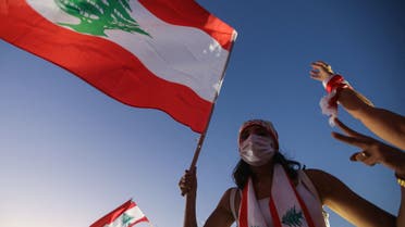 A Lebanese protester lifts a national flag during a demonstration marking the one year anniversary of the beginning of a nationwide anti-government protest movement, in the capital Beirut on October 17, 2020. Hundreds marched in Lebanon's capital to mark the first anniversary of a non-sectarian protest movement that has rocked the political elite but has yet to achieve its goal of sweeping reform.