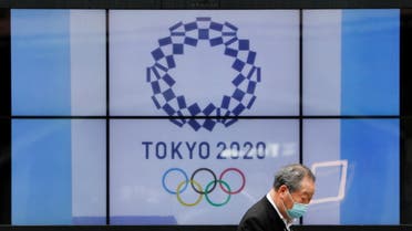 A passerby wearing a protective face mask walks past a screen showing the logo of the 2020 Olympic Games in Tokyo, Japan, April 14, 2021. (Reuters)
