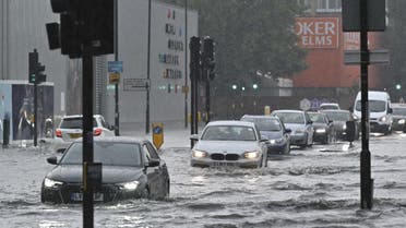 Cars drive through deep water on a flooded road in The Nine Elms district of London on July 25, 2021 during heavy rain. Buses and cars were left stranded when roads across London flooded on Sunday, as repeated thunderstorms battered the British capital. (AFP)