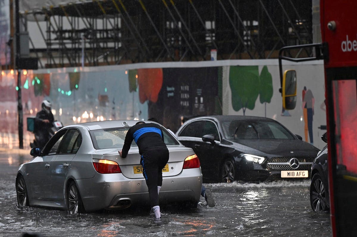 A person pushes a broken-down car through deep water on a flooded road in The Nine Elms district of London on July 25, 2021 during heavy rain. Buses and cars were left stranded when roads across London flooded on Sunday, as repeated thunderstorms battered the British capital. (AFP)