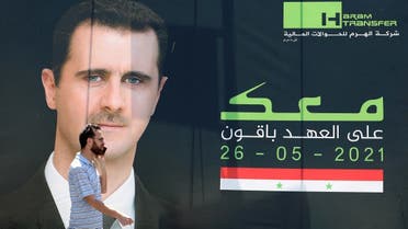 A man talks on his mobile phone as he walks past an election campaign billboard depicting Syrian President Bashar al-Assad, a candidate for the upcoming presidential vote, in the capital Damascus on May 23, 2021. (AFP)