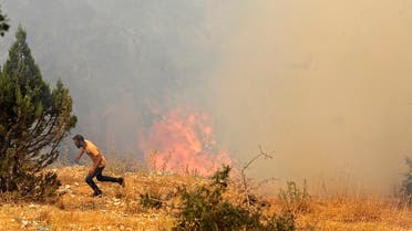 A man runs for cover as Lebanese firemen douse the flames in the forests of the Qoubaiyat area in northern Lebanon's Akkar, July 29, 2021. (AFP)