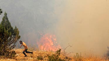 A man runs for cover as Lebanese firemen douse the flames in the forests of the Qubayyat area in northern Lebanon's remote Akkar region on July 29, 2021. (File photo: AFP)