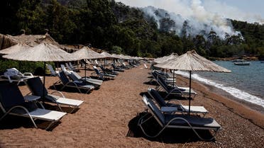 An empty beach is seen as smoke rises from a forest during a wildfire near Marmaris, Turkey, August 3, 2021. (Reuters/Umit Bektas)