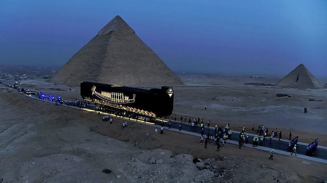 This handout picture released by the Egyptian Ministry of Antiquities on August 7, 2021 shows a view of the relocation process of the Solar Barque of Pharaoh Khufu (Cheops) as it is moved past (L to R) the Pyramid of Khafre (Chephren) and Menkaure (Menkheres) from the Giza Necropolis to its new resting place at the nearby Grand Egyptian Museum (GEM) on the outskirts of the Egyptian capital's twin city of Giza. Egypt on August 7 transported the intact Pharaonic boat of ancient Egyptian King Khufu dating back some 4600 years to its yet to be unveiled grand museum. (AFP)