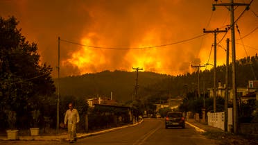 A local resident walks as a wildfire rages near the village of Gouves, on Euboea island, second largest Greek island, on August 8, 2021. Hundreds of firefighters battled a blaze on the outskirts of Athens as several fires raged in Greece.