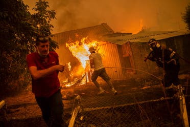 A firefighter and locals rush to a burning house in an attempt to extinguish forest fires that are approaching the village of Pefki on Evia (Euboea) island, Greece's second largest island, on August 8, 2021. (AFP)
