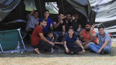 Migrants react to the camera as they sit by a tent in a camp near the border town of Kapciamiestis, Lithuania, on July 18, 2021. (Petras Malukas/AFP)