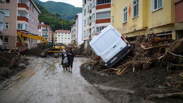 A man and woman walk along a muddy street after flash floods destroyed parts of Bozkurt in the district of Kastamonu, in the Black Sea region of Turkey on August 14, 2021. (STR/AFP)