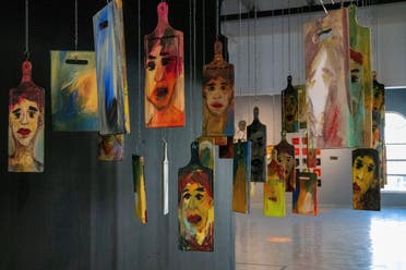 A hanging array of chopping boards that have faces painted on them.