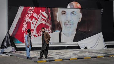 Afghan men stand next to a torn poster of Afghan President Ashraf Ghani at the Kabul airport in Kabul on August 16, 2021. (Wakil Kohsar/AFP)