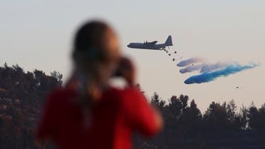 A person films an Israeli Air Force C-130 Hercules cargo airplane dropping flame retardant to fight a wildfire on the outskirts of Jerusalem, on  August 17, 2021.  (AP)