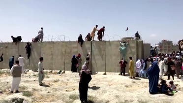 People climb a barbed wire wall to enter the airport in Kabul, Afghanistan August 16, 2021, in this still image taken from a video. REUTERS TV/via REUTERS