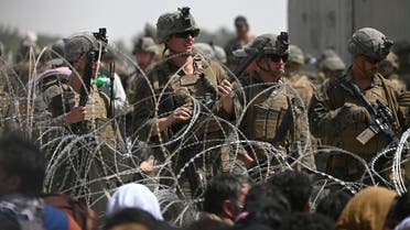 US soldiers stand guard behind barbed wire as Afghans sit on a roadside near the military part of the airport in Kabul on August 20, 2021, hoping to flee from the country after the Taliban's military takeover of Afghanistan. (AFP)