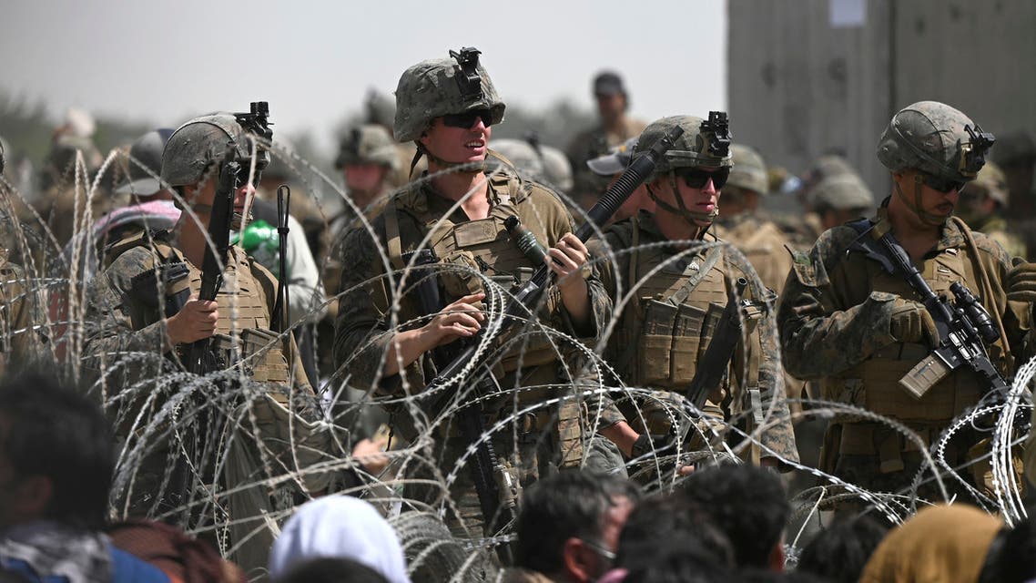 US soldiers stand guard behind barbed wire as Afghans sit on a roadside near the military part of the airport in Kabul on August 20, 2021, hoping to flee from the country after the Taliban's military takeover of Afghanistan.