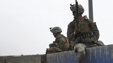 US soldiers sit on a wall as Afghans gather on a roadside near the military part of the airport in Kabul on August 20, 2021. (AFP)