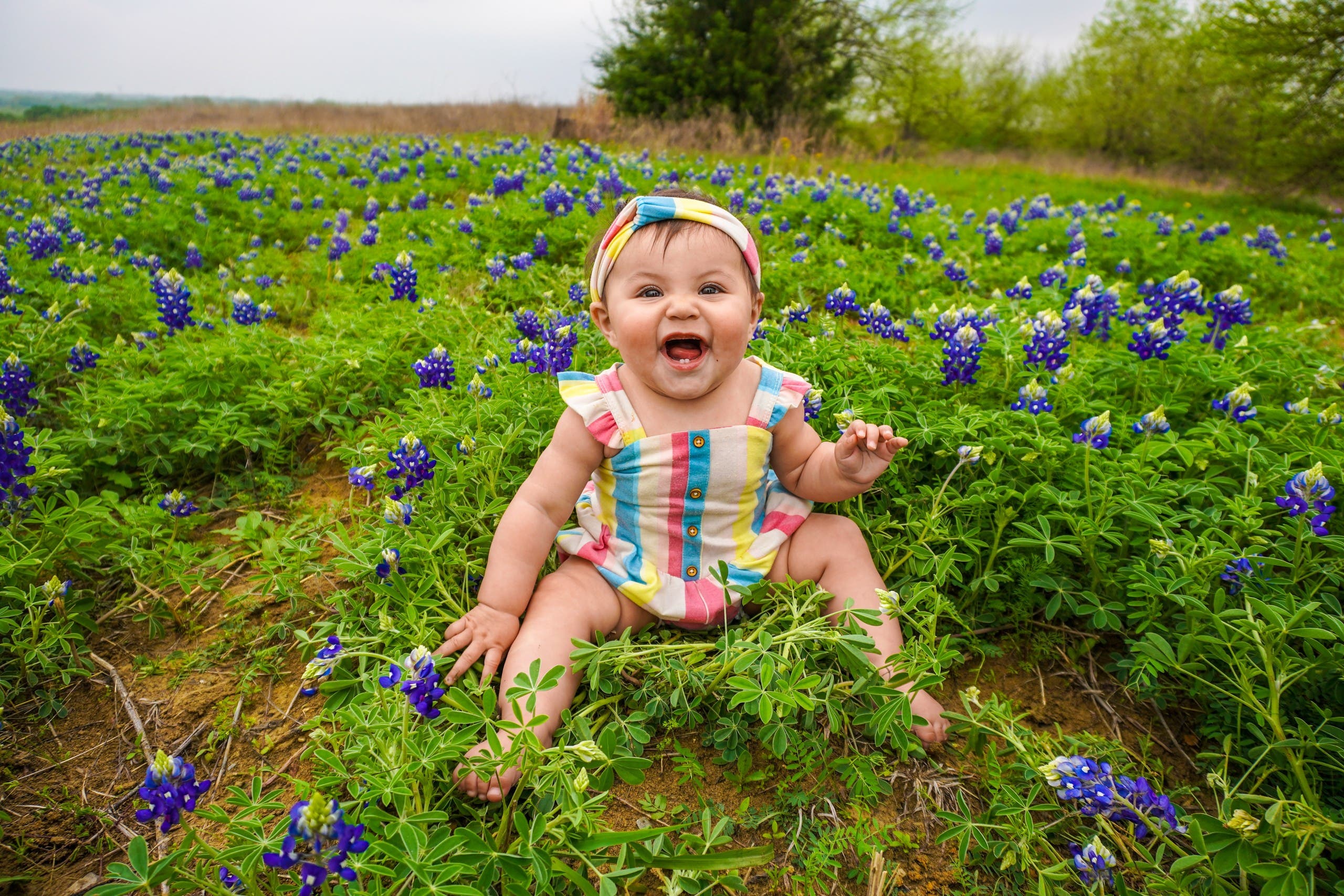 A baby is pictured sitting on grass and laughing. (Unsplash, Danny de los Reyes)