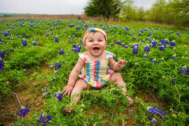 A baby is pictured sitting on grass and laughing. (Unsplash, Danny de los Reyes)