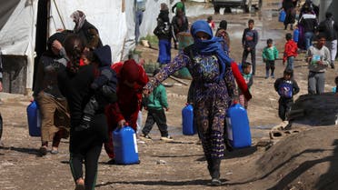 Syrian refugees walk as they carry containers at an informal tented settlement in the Bekaa valley, Lebanon March 12, 2021. (Reuters)