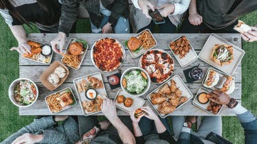 People sitting at a table with food on the grass. (Unsplash, Spencer Davis)