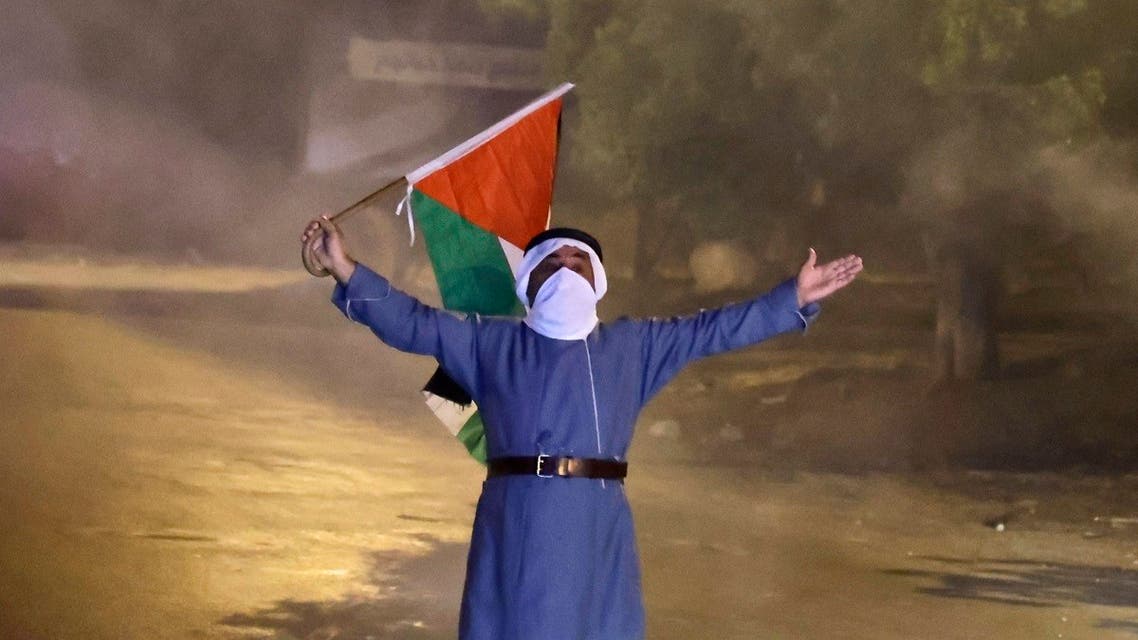 A Palestinian man waves his national flag near the Israeli-controlled Hawara checkpoint during clashes with Israeli forces following a protest in support of the six Palestinian prisoners who escaped from Israel’s Gilboa prison, on September 13, 2021. (Jaafar Ashtiyeh/AFP)