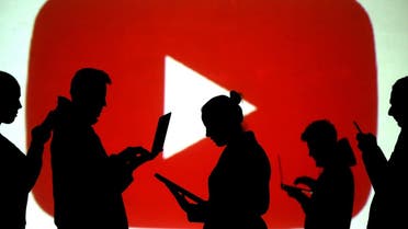 Silhouettes of laptop and mobile device users are seen next to a screen projection of the YouTube logo. (Reuters)