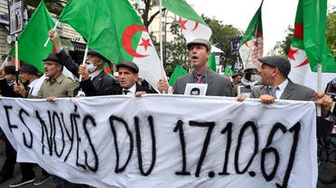People hold a banner and Algerian flags during a rally to commemorate the brutal repression of an Oct 17, 1961 demonstration during which at least 120 Algerians were killed during a protest to support Algerian independence, near the Pont Neuf bridge on October 17, 2021 in Paris. (AFP)