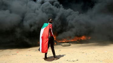 FILE PHOTO: FILE PHOTO: A person wearing a Sudan's flag stand in front of a burning pile of tyres during a protest against prospect of military rule in Khartoum, Sudan October 21, 2021. REUTERS/Mohamed Nureldin Abdallah//File Photo/File Photo