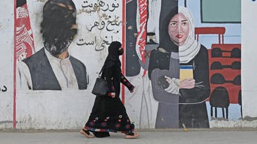 A woman walks past a mural painted on the wall along a road in Mazar-i-Sharif on October 31, 2021. (Photo by WAKIL KOHSAR / AFP)