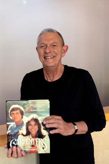 Richard Carpenter smiles as he poses with his new book: “Carpenters: The Musical Legacy,” at his home in Thousand Oaks, California, on Sept. 10, 2021. (Reuters)