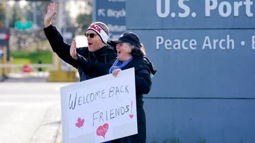 Dual US-Canadian citizen Traysi Spring (right), and her American husband Tom Bakken, hold a homemade sign to welcome people heading into the US from Canada on Nov. 8, 2021, in Blaine, Washington. (AP)