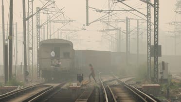 A woman crosses railway tracks as a goods train passes by, on a smoggy day in New Delhi, India, on November 12, 2021. (Reuters)