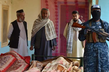 عنصر من طالبان وسكان من قندهار أمام جثتي مدنيين قضيا خلال المعارك مع داعش اليوم