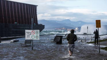 A pedestrian walks along a flooded sea wall past a barge that came loose from its mooring after rainstorms lashed the western Canadian province of British Columbia in Vancouver, British Columbia, Canada, on November 15, 2021. (Reuters)