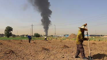 Farmers work in a field as smoke from an oil refinery rises in the background, in Tehran, Iran June 3, 2021. (Reuters)