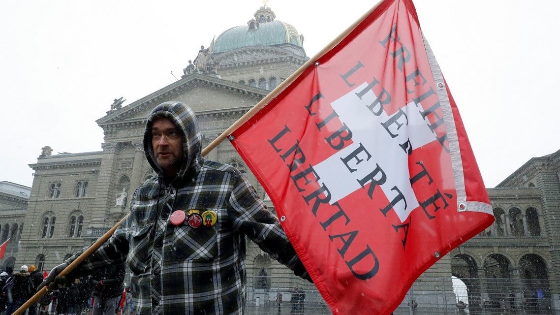 A demonstrator holds a Swiss flag with the word freedom in several languages during a protest against a coronavirus disease (COVID-19) law that is voted on in a referendum, in front of the Swiss Federal Palace, the Bundeshaus, in Bern, Switzerland. (Reuters)