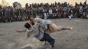 Afghan men wrestle as spectators watch in the background during a weekly spectacle of wrestling held in a makeshift arena at Chaman-e-Hozori park, in Kabul City, on November 12 2021. (Photo by Hector RETAMAL / AFP)