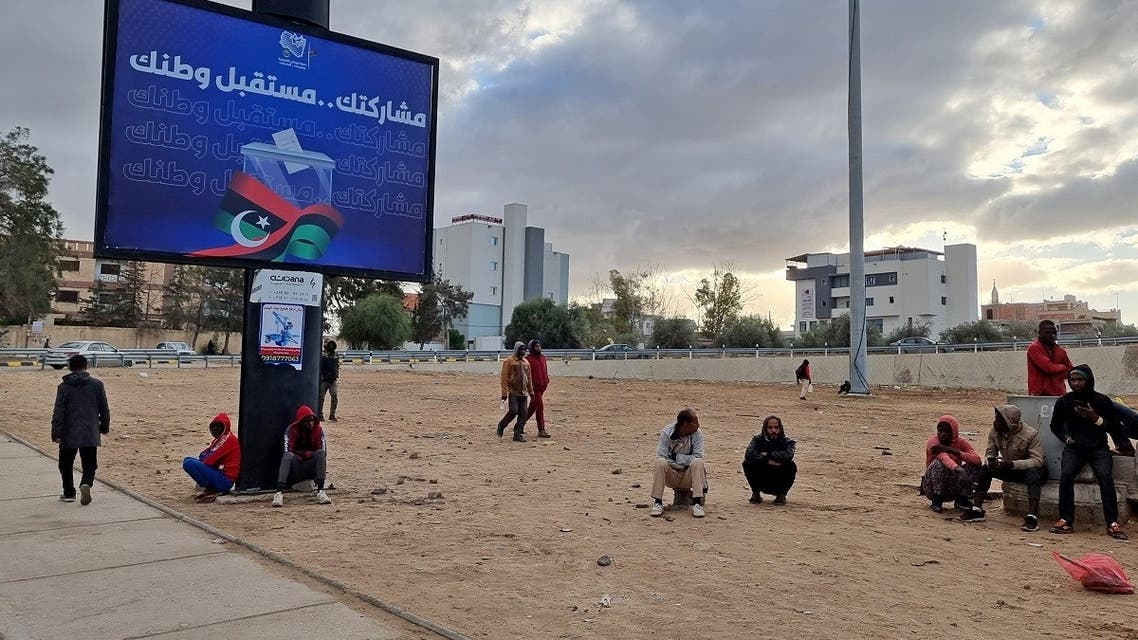 Workers sit near an electoral billboard reading in Arabic “your participation is the future of your country” in Libya’s capital Tripoli on December 14, 2021. (AFP)
