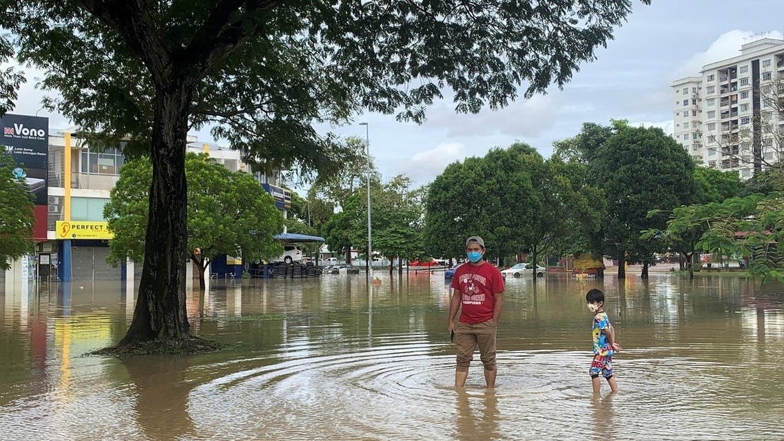A man and his child stand in flood water in Shah Alam, Selangor state, Malaysia, on December 19, 2021. (Reuters)