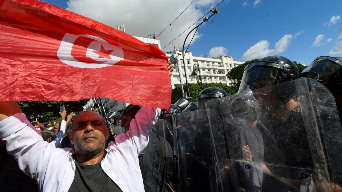 A Tunisians man holding a national flag stands in front of riot police during a rally against their president along the Habib Bourguiba avenue in the capital Tunis, on October 10, 2021. (AFP)