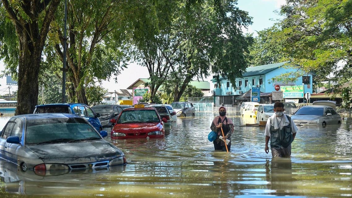 People walk past cars partially submerged in floodwaters in Shah Alam, Selangor on December 21, 2021, as Malaysia faces massive floods that have left at least 14 dead and more than 70,000 displaced. (Photo by Arif KARTONO / AFP)