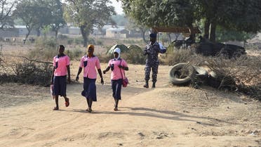 A policeman walk behind school girls as they cross the border in Yemboate, the northern Togo border post with Burkina Faso, on February 17, 2020. (AFP)