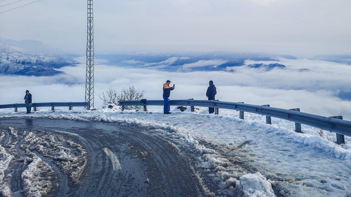 A file photo shows people take pictures of the winter snow with their mobile phones at a curve along a road in Pir Chinasi, a hilly area of Muzaffarabad on December 28, 2021. (AFP)