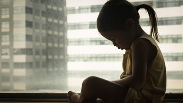 A litte girl sitting next to a window with her head down in sadness. Feeling depressed and hurt. Sad child cryng alone. Depression. stock photo