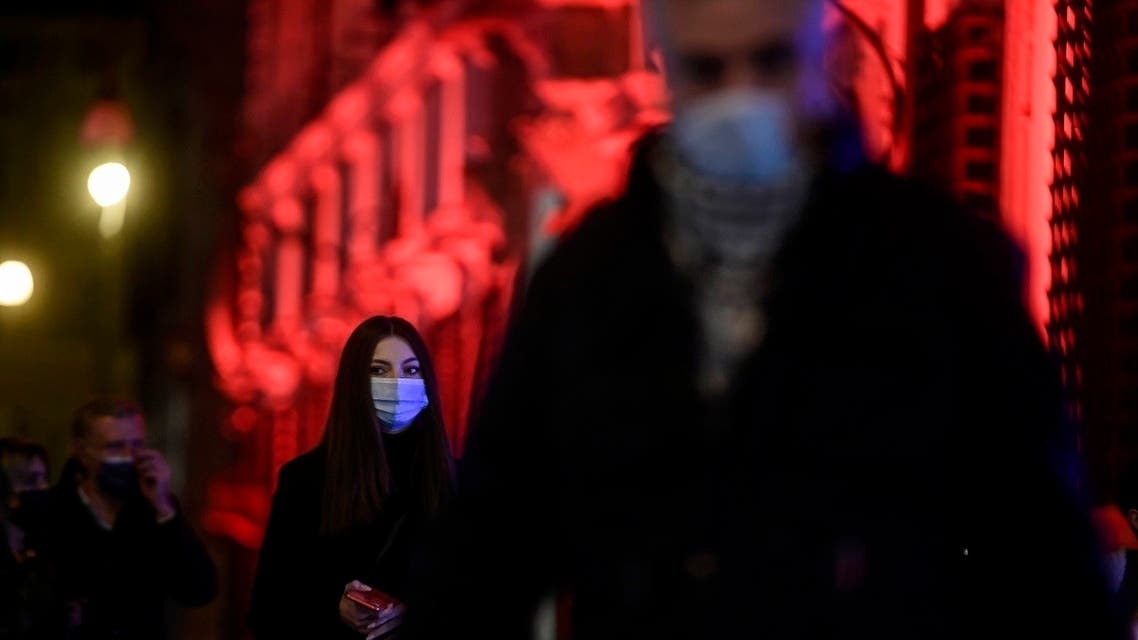 A woman wearing a face mask walks past the Italian government's Chigi palace illuminated in red on the occasion of the International Day for the Elimination of Violence against Women, on November 25, 2020 in Rome. (AFP)