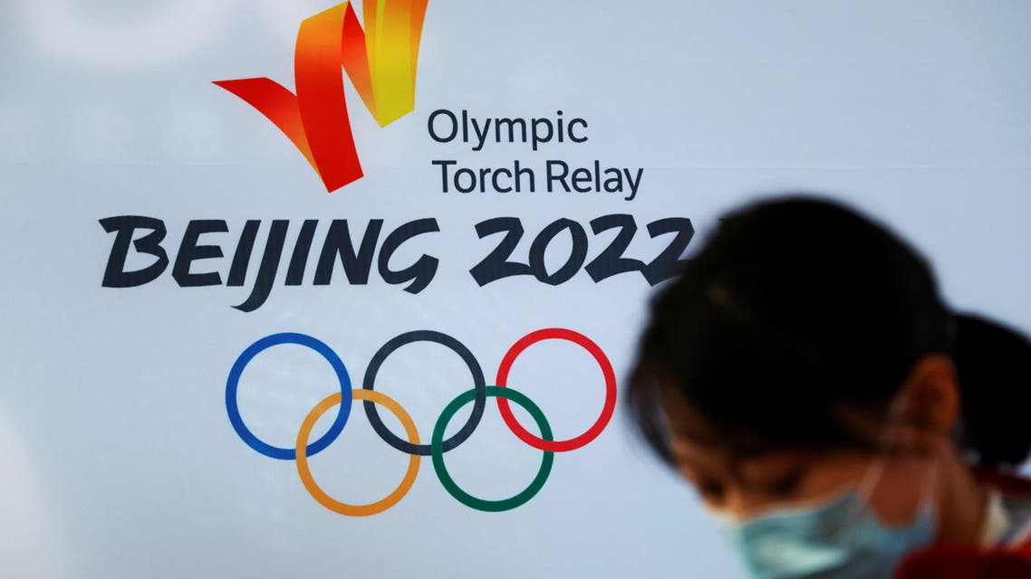 A woman wearing a face mask stands in front of the logo of the Beijing 2022 Winter Olympics before the Olympics flame exhibition tour at Beijing University of Posts and Telecommunications, in Beijing, China December 9, 2021. REUTERS/Carlos Garcia Rawlins